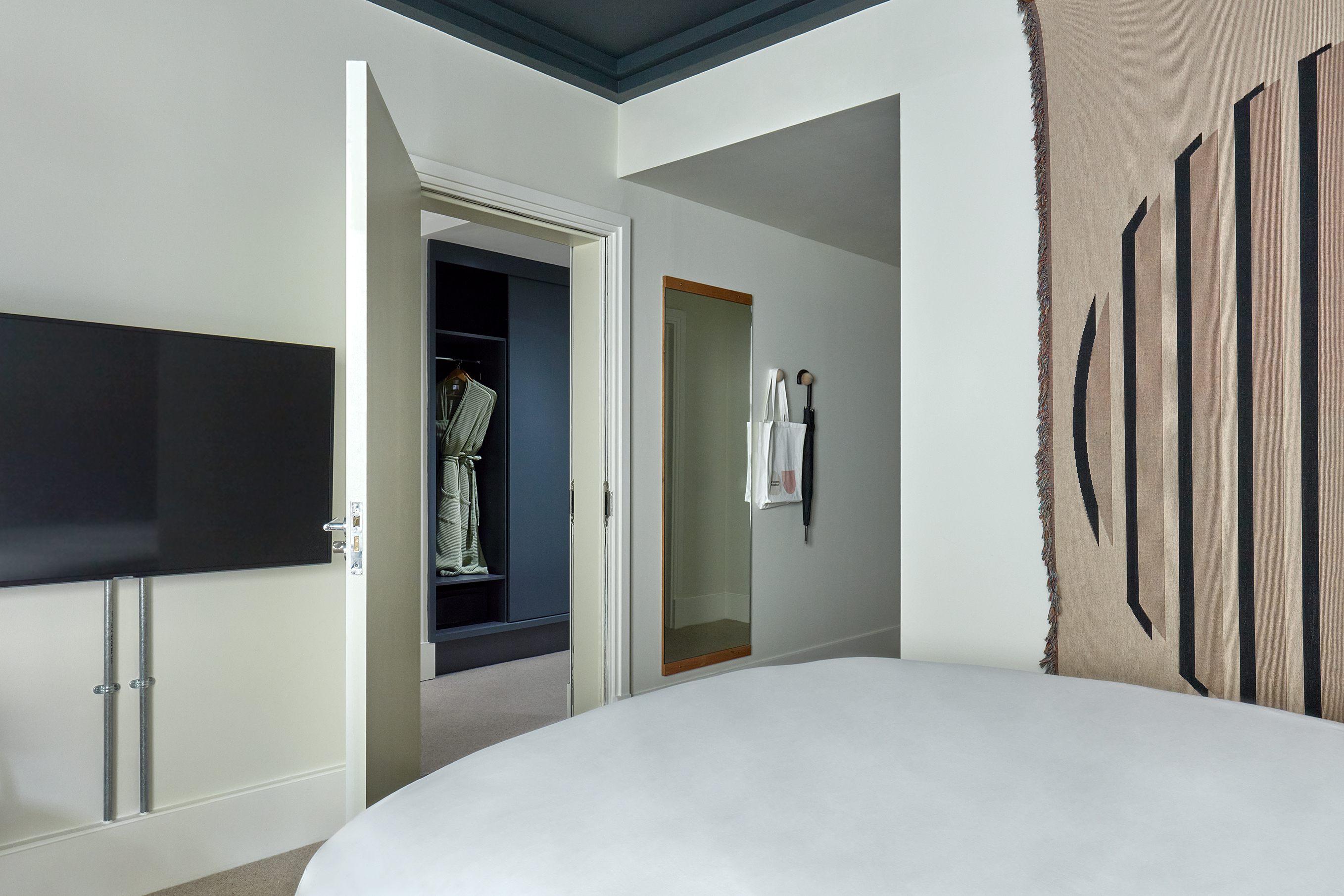Bedroom at One Hundred Shoreditch with a striped tapestry, adjacent to an open closet displaying a robe.