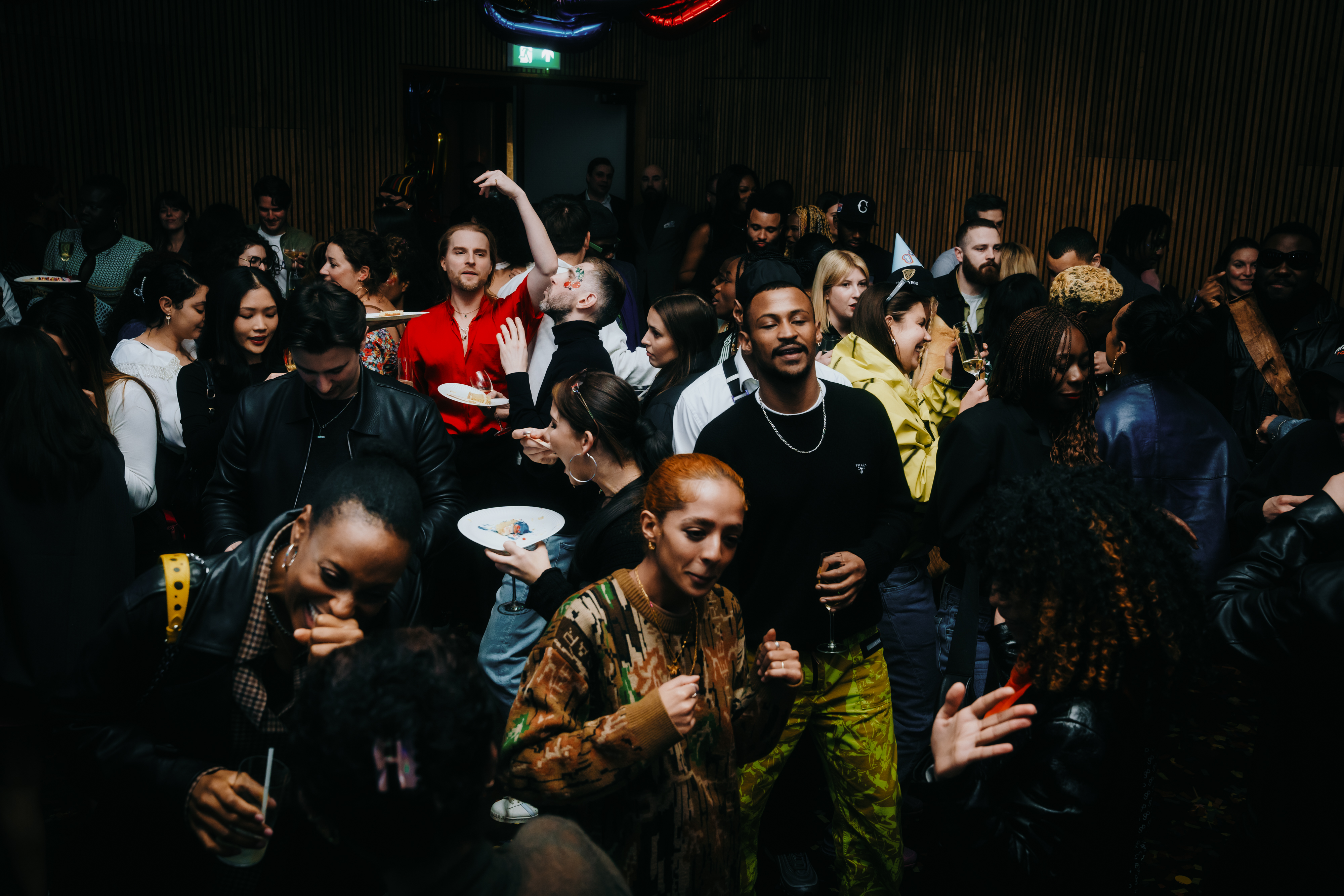 Party-goers enjoying a crowded indoor event in London with drinks, vibrant outfits, and a lively atmosphere.