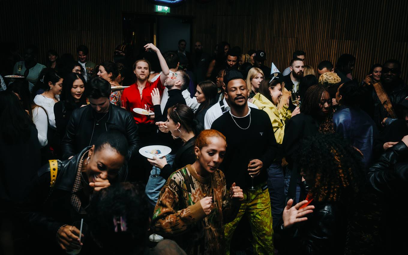 Party-goers enjoying a crowded indoor event in London with drinks, vibrant outfits, and a lively atmosphere.