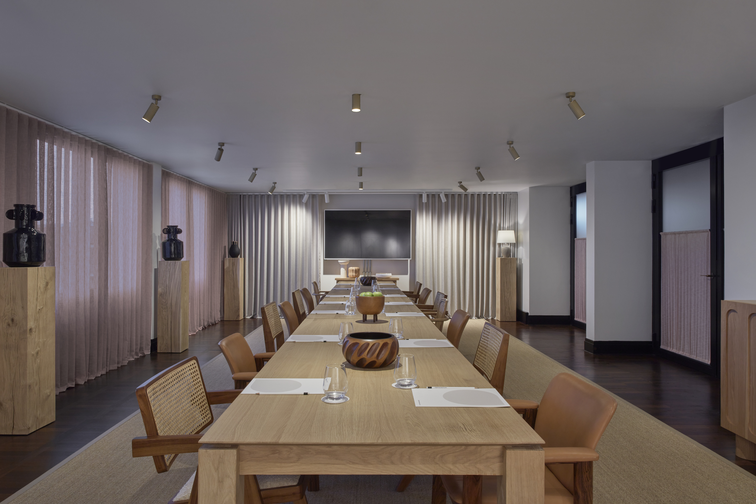A long table surrounded by chairs, featuring a lamp positioned centrally on the table.
