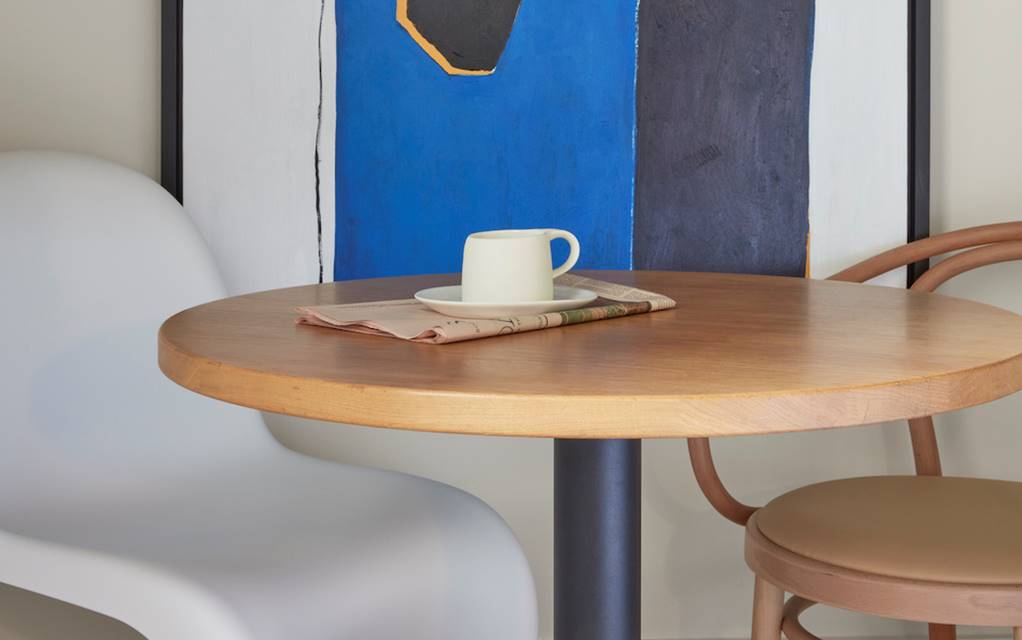 A round table with two chairs positioned beside a colourful painting on the wall.