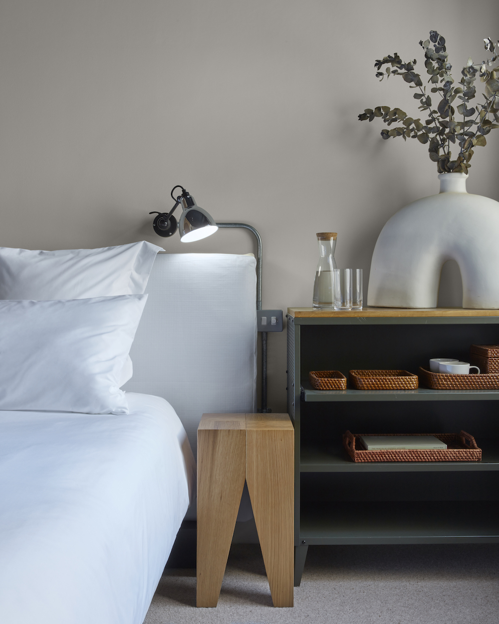 A neatly made bed with white sheets and a decorative vase placed on a night stand, creating a serene and inviting atmosphere.