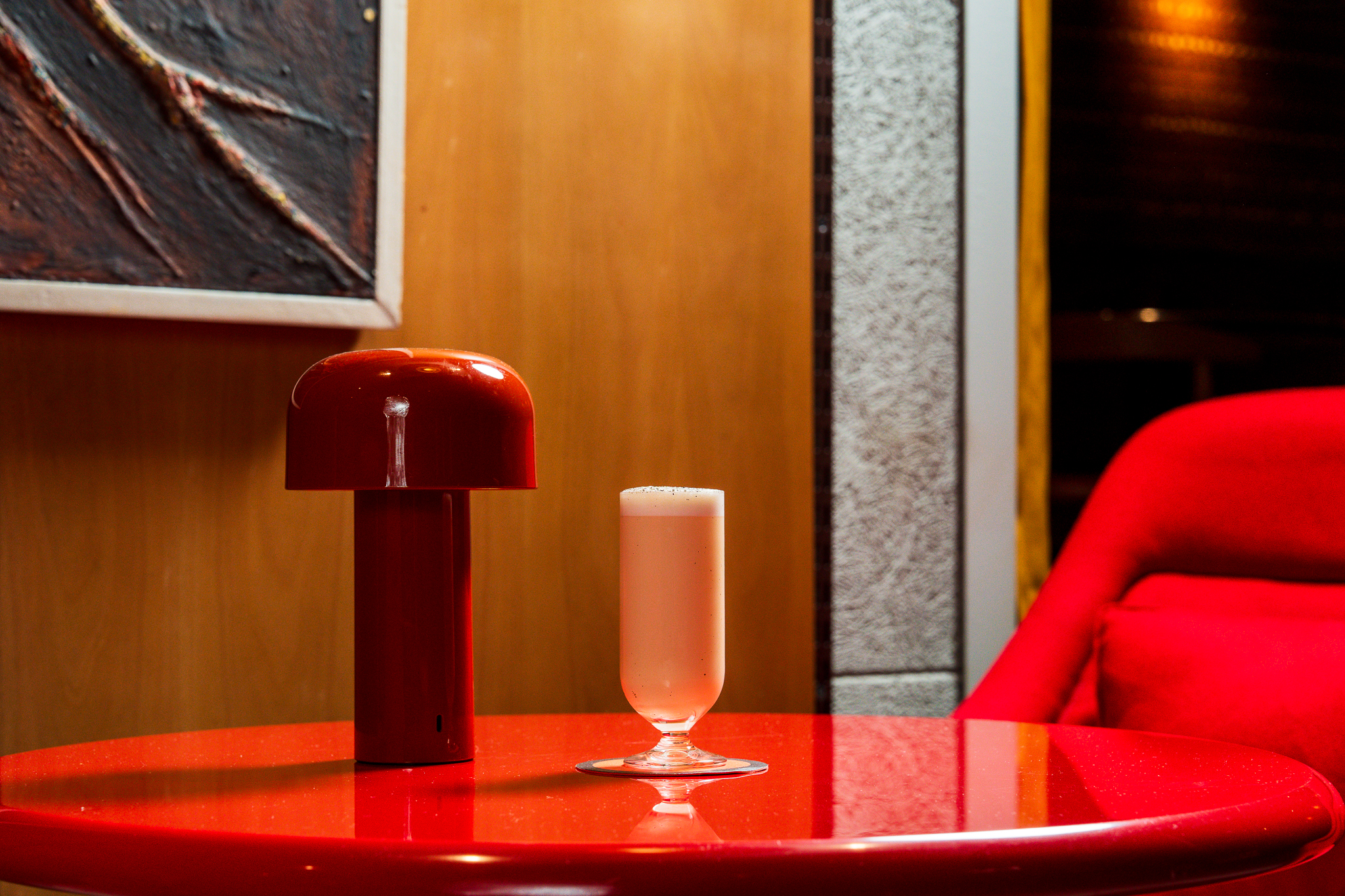 A red table with a mushroom-shaped lamp and a creamy cocktail in a sleek, modern setting at a London bar.