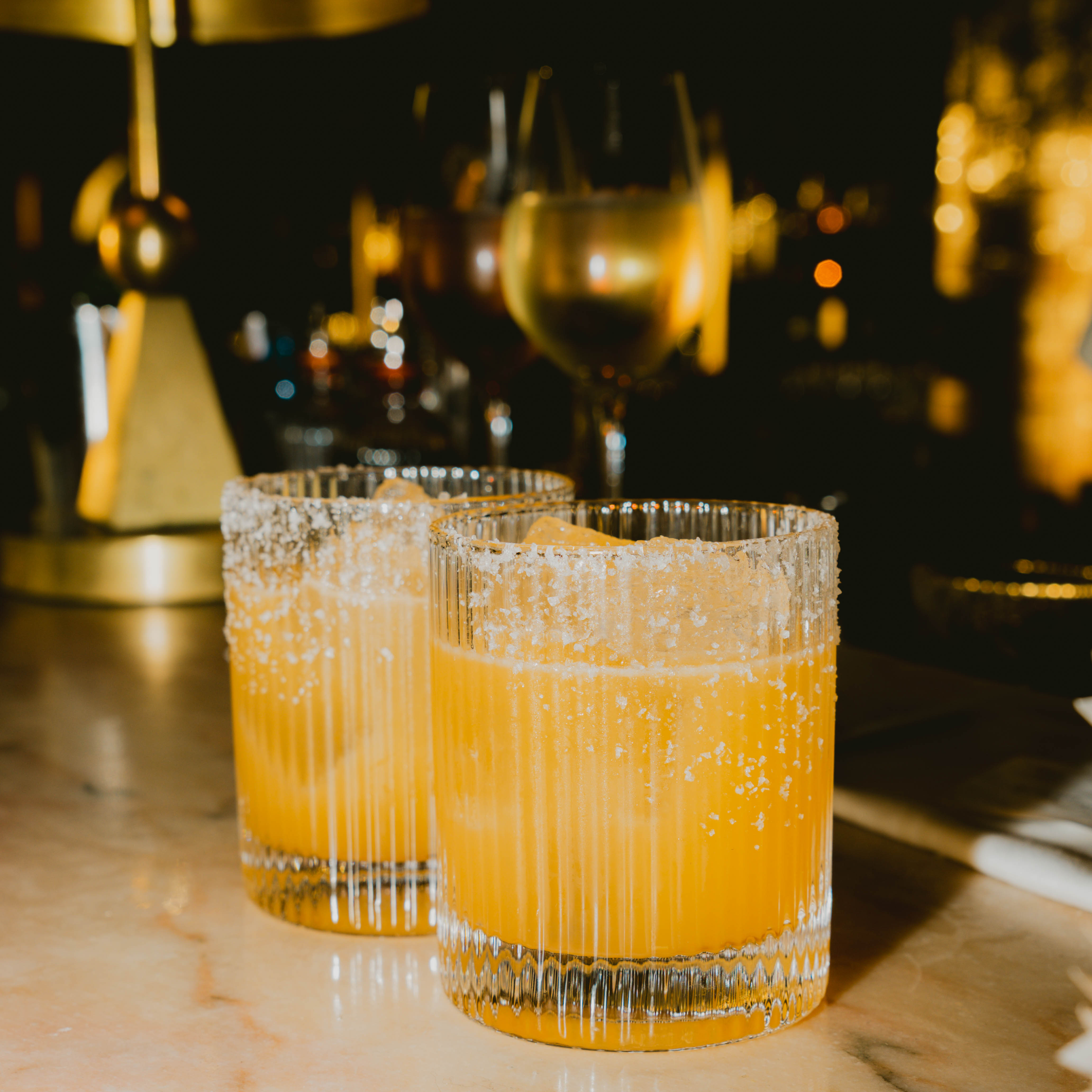 Two glasses of vibrant orange drink placed on a polished bar surface, inviting and refreshing in appearance.