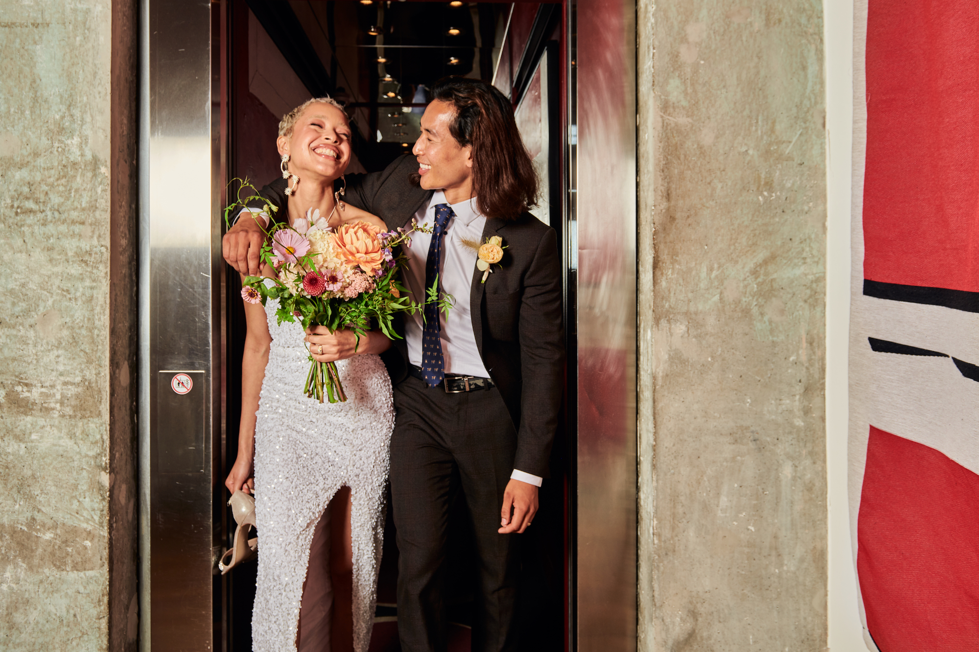 A bride and groom smile together for a photo inside a stylish elevator, capturing a moment of joy on their wedding day.