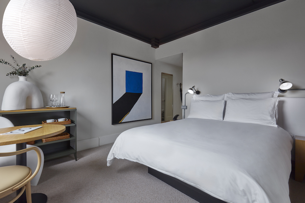 A modern and welcoming bedroom featuring a bed, a table, and a decorative painting on the wall.