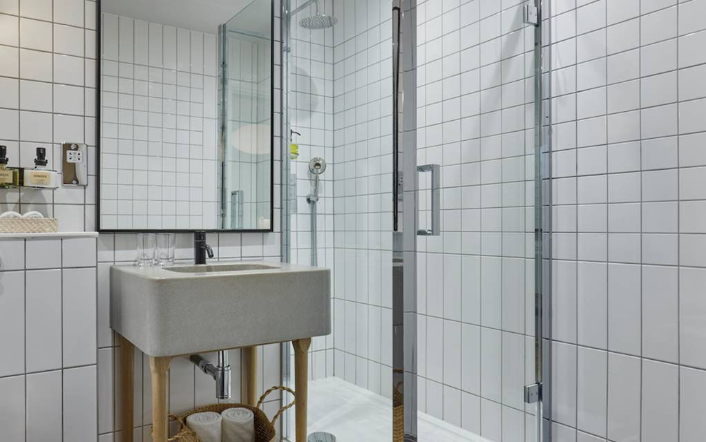 Bathroom with white tiles, glass shower door, and wooden accents, creating a clean, modern aesthetic in a London hotel room.