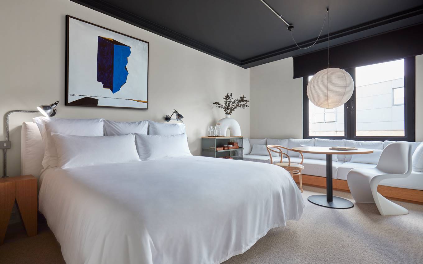 A serene bedroom featuring a white bed and an elegant painting adorning the wall, creating a tranquil atmosphere.