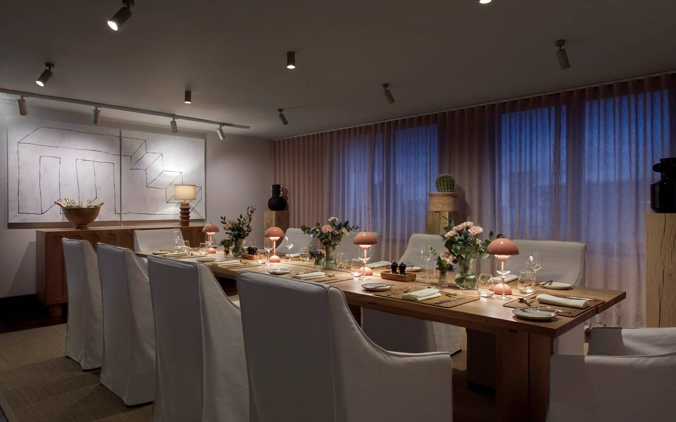 A private dining setup in London with a long table, white chairs, pink lamps, and fresh flowers, set for an intimate dinner.