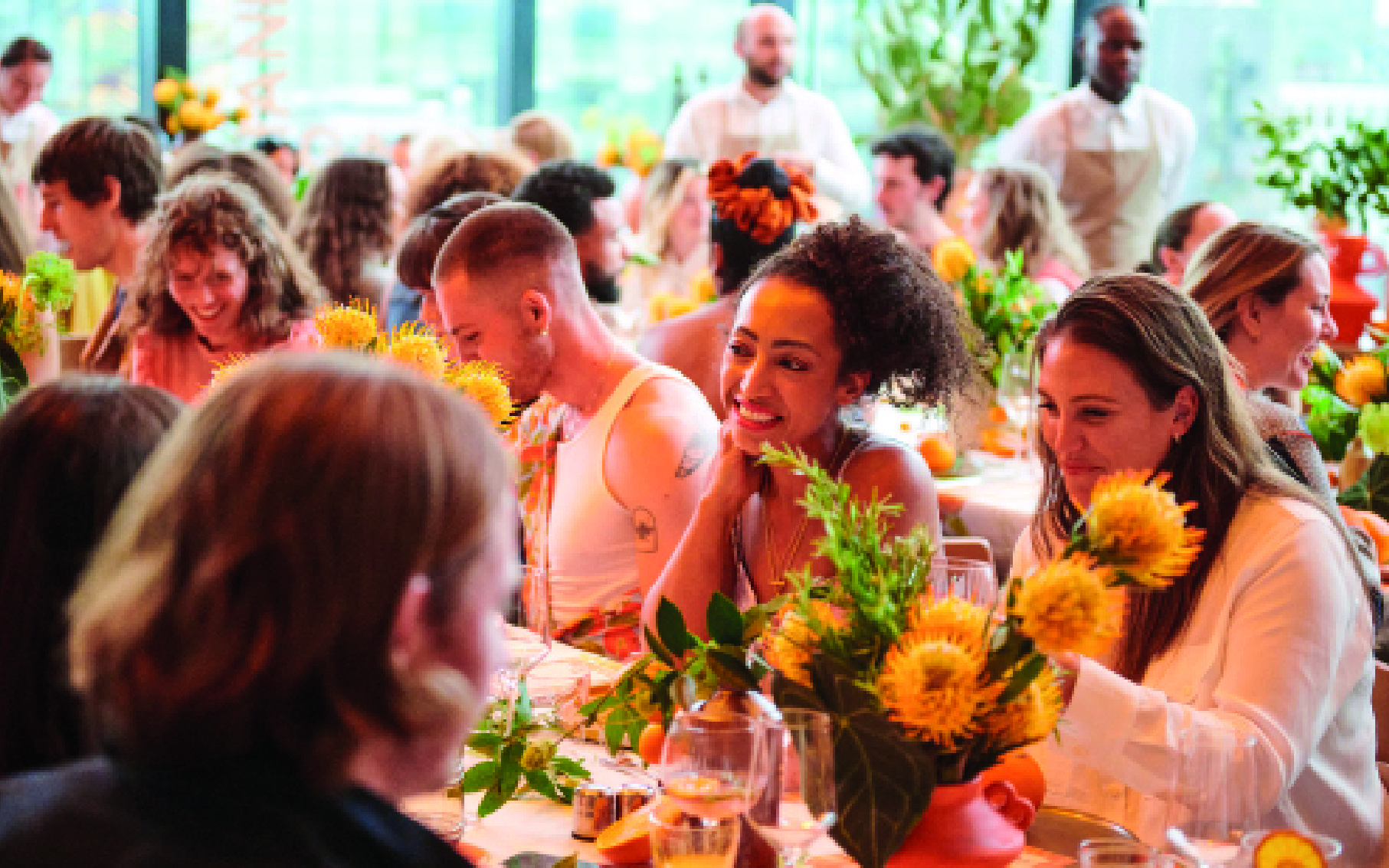 A gathering of individuals seated at tables adorned with vibrant sunflowers, enjoying a sunny day together.