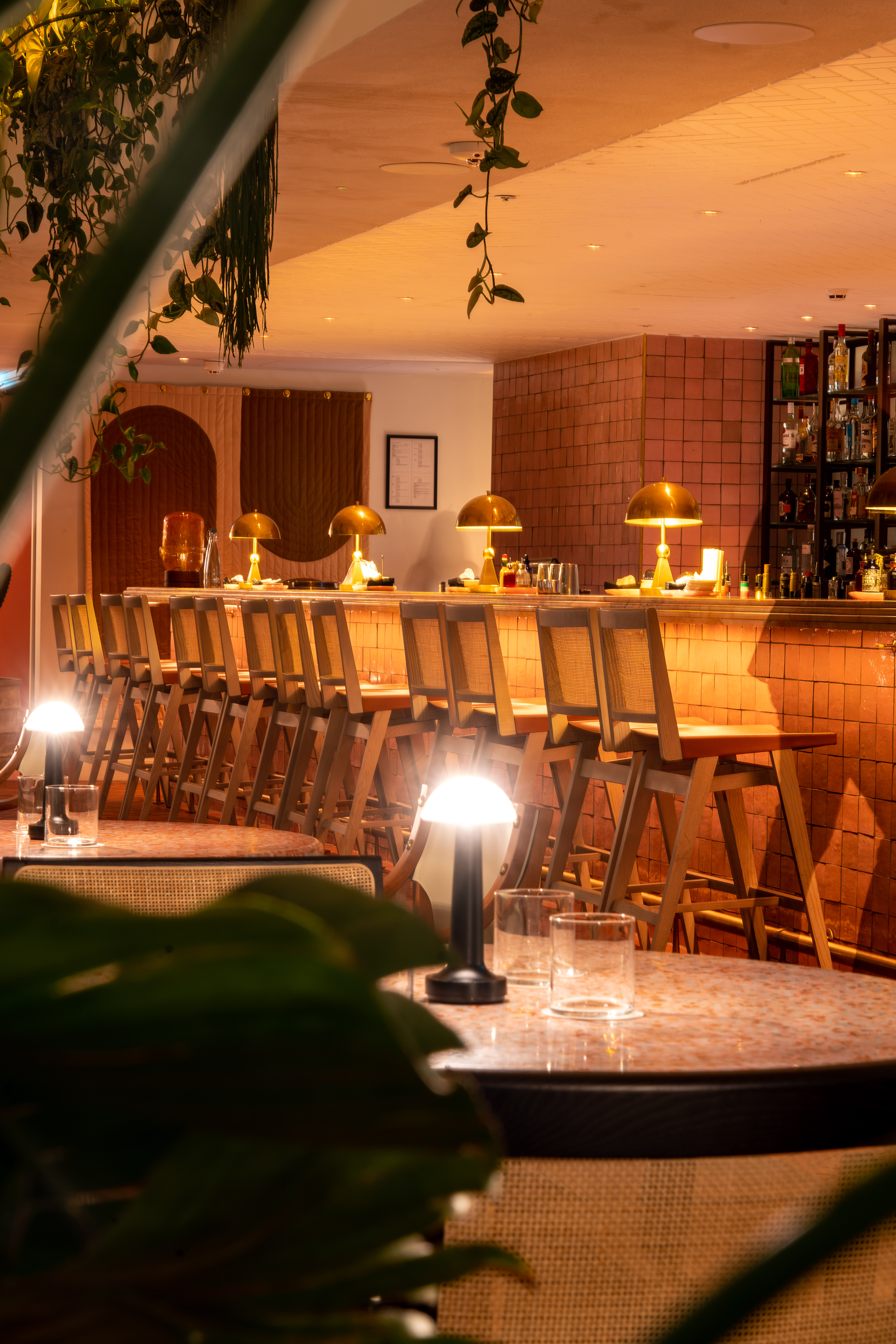 A long wooden bar featuring stools and decorative lamps, creating a warm and inviting atmosphere.