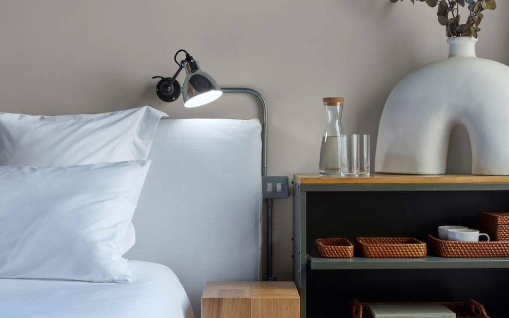 A neatly made bed with white sheets and a decorative vase placed on a night stand, creating a serene and inviting atmosphere.