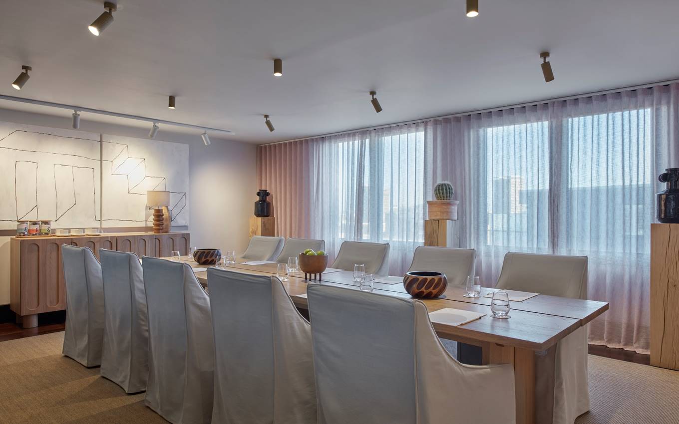 A modern meeting room in London with a large wooden table, white slipcovered chairs, abstract wall art, and natural light.
