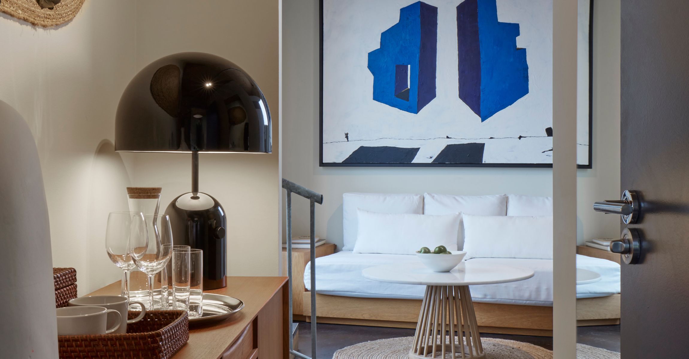 Close-up of a room setup with a sleek black lamp, glassware, and a bold blue abstract painting in the background.