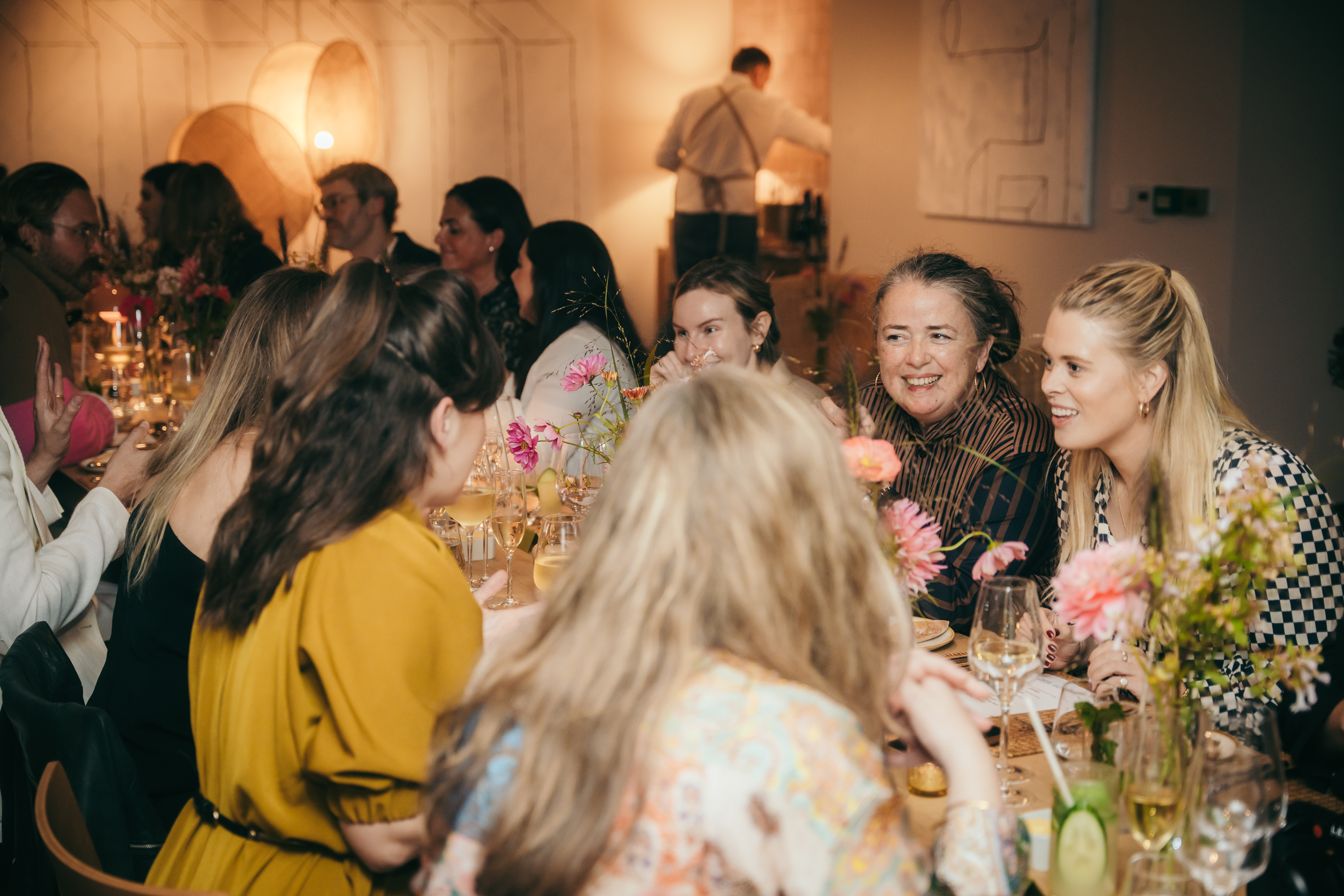 A group of women gathered around a table adorned with flowers, engaged in conversation and enjoying each other's company.