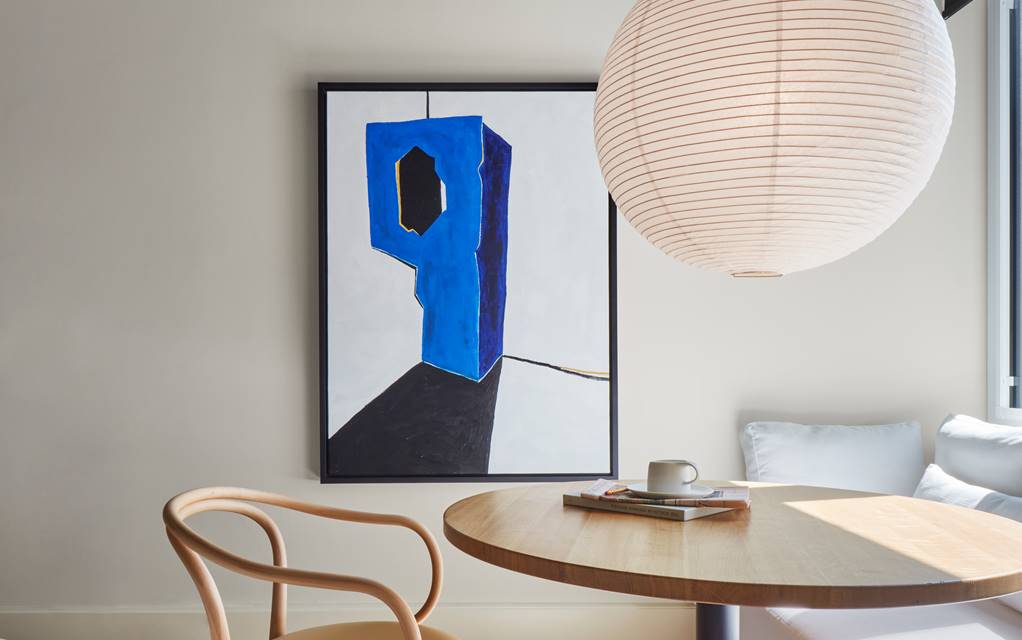 Cosy dining nook with a round wooden table, a modern chair, and abstract blue artwork on the wall.