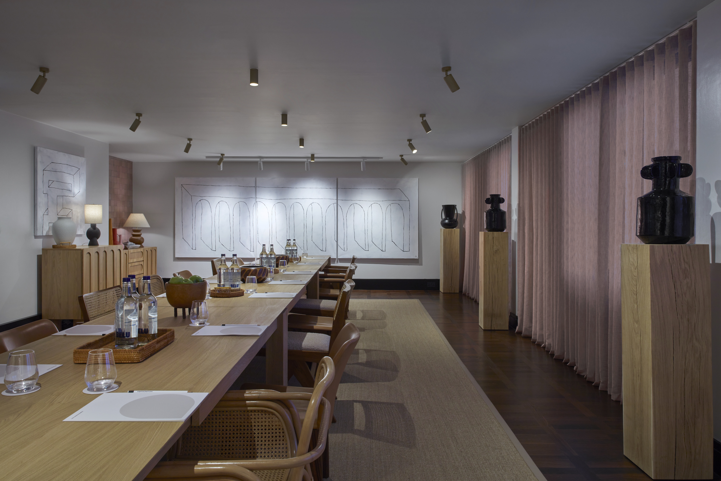 A beautifully arranged meeting room setup featuring modern art pieces, and a wooden boardroom table, bathed in soft light.