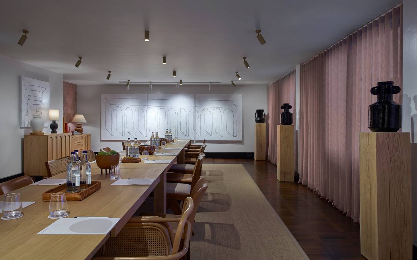 A beautifully arranged meeting room setup featuring modern art pieces, and a wooden boardroom table, bathed in soft light.