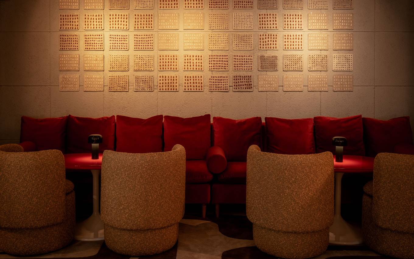 Lounge area with red sofa, cosy chairs, and textured wall art at the Seed Library cocktail bar in London.