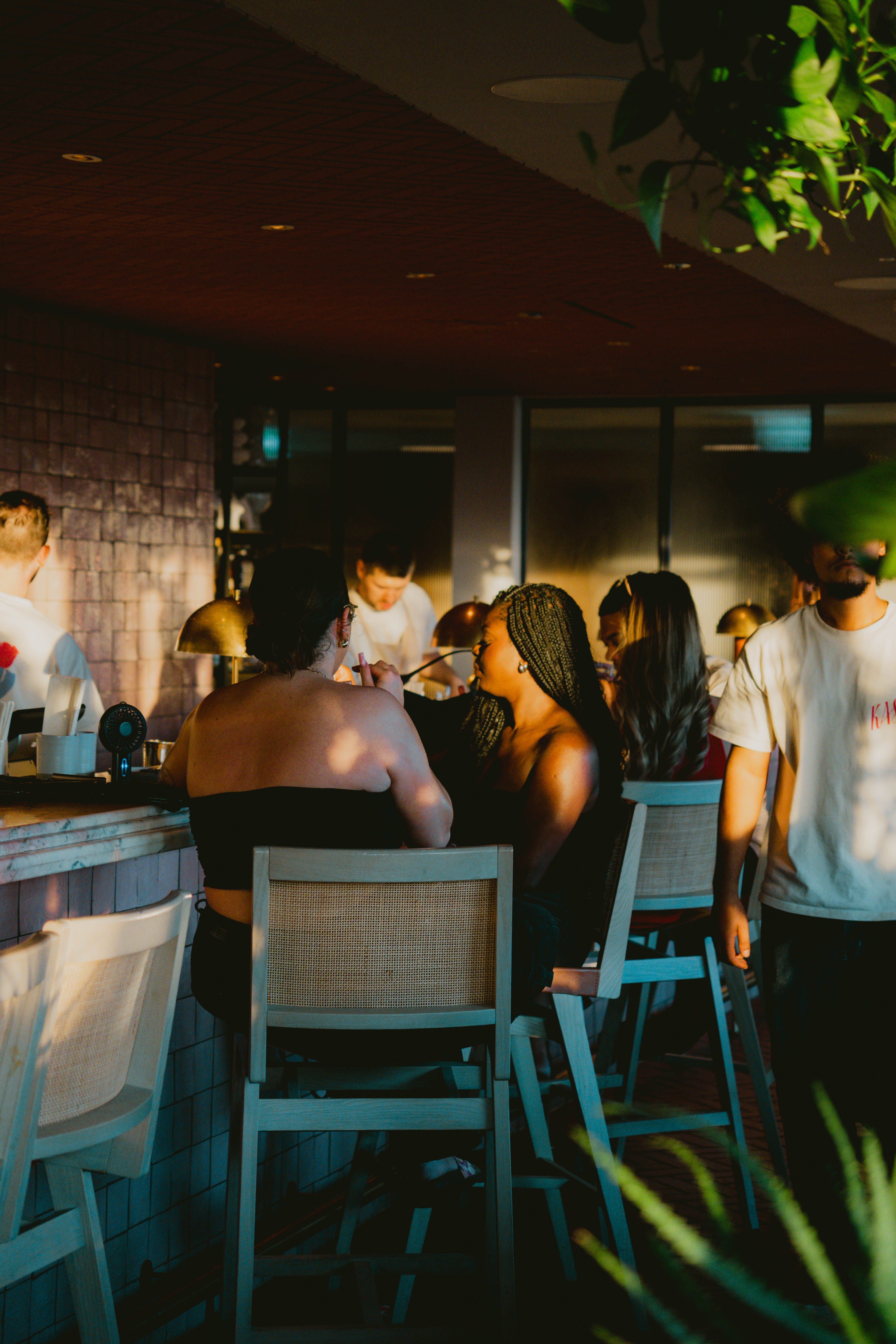 A lively bar scene featuring people socialising, with a woman seated on the bar, creating a vibrant atmosphere.