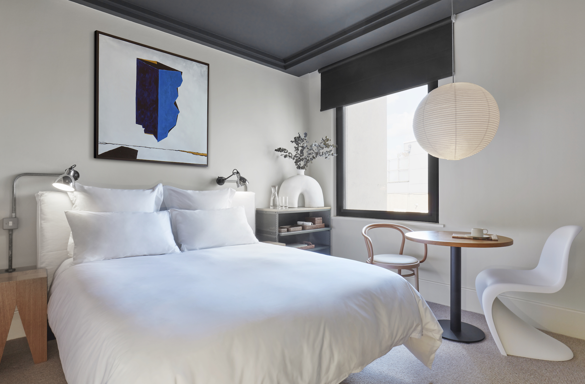 A serene bedroom featuring a white bed and an elegant painting adorning the wall, creating a tranquil atmosphere.