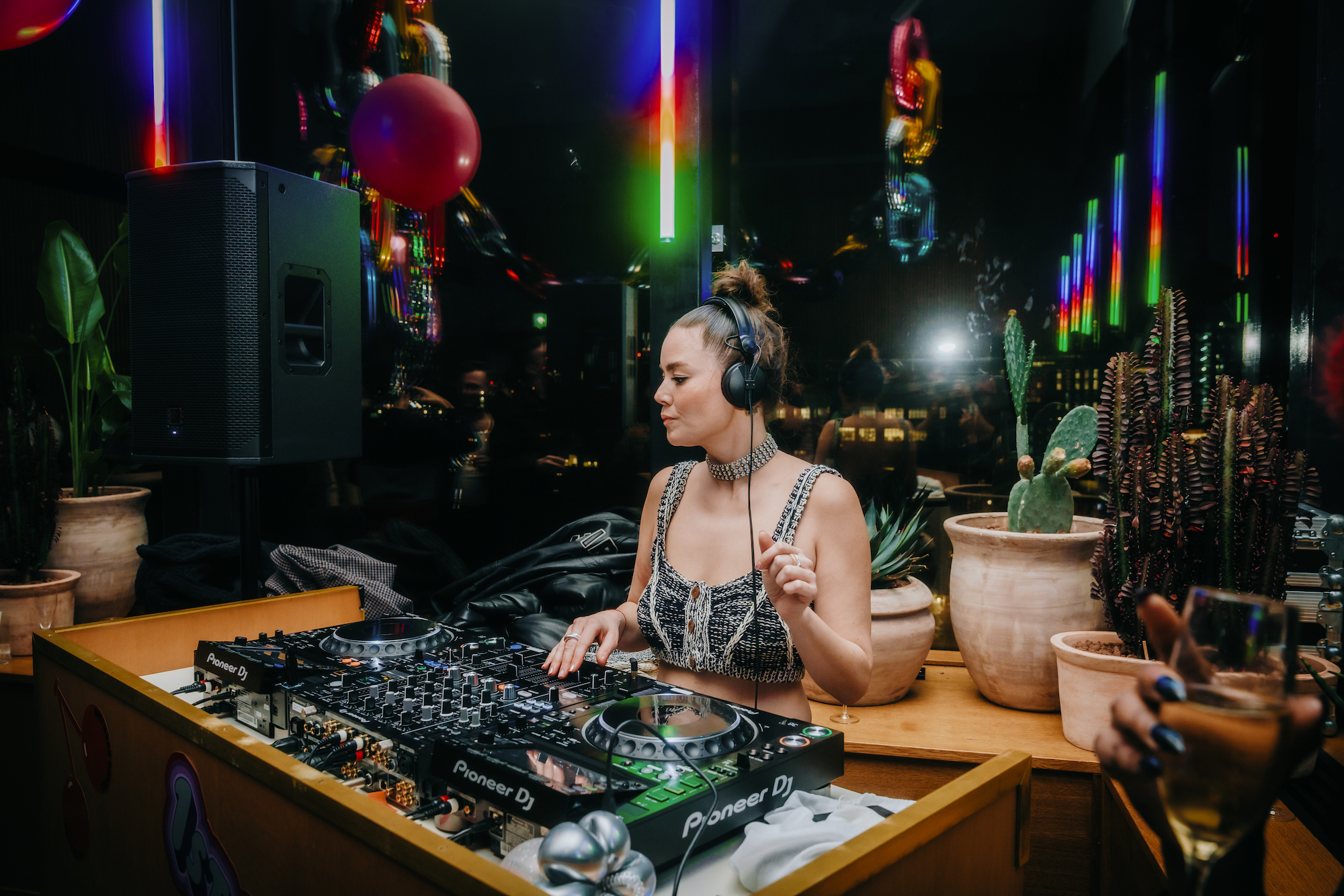 A DJ playing on a mixer, surrounded by neon lights and balloons, creating an upbeat atmosphere for a London party.
