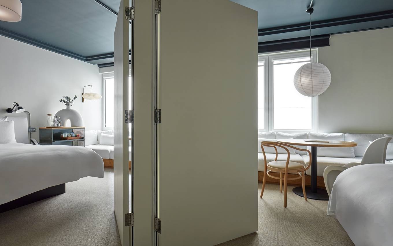 Divided hotel suite at One Hundred Shoreditch with bed, seating area, and round table, separated by a door for privacy.